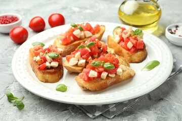 Tasty bruschettas with mozzarella cheese, tomatoes, basil and spices on grey textured table, closeup