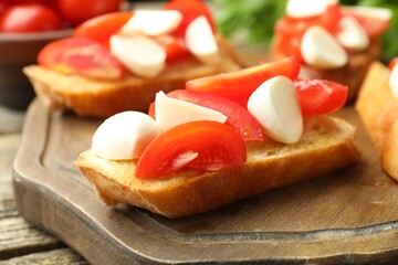 Tasty bruschettas with mozzarella cheese and tomatoes on wooden table, closeup