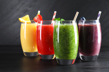 Different tasty smoothies in glasses with ingredients on black wooden table