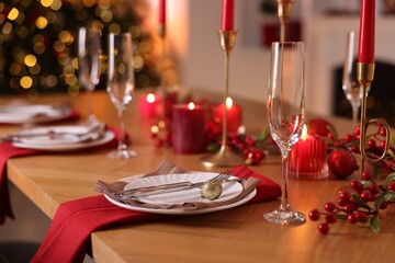 Stylish Christmas table setting with plates, glasses and burning candles in festive decorated room, closeup. Bokeh effect