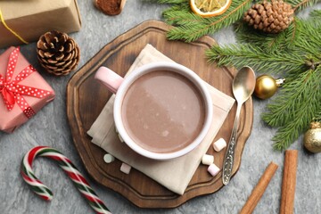 Tasty cocoa, marshmallows, cinnamon, candy cane and Christmas decor on grey table, flat lay
