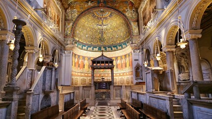 Rome, Italy - 11 January 2025. Interior of San Clemente with carved marble seating, archways, a wooden baldachin over the altar, and golden mosaics above rows of saints and sheep. © Michael