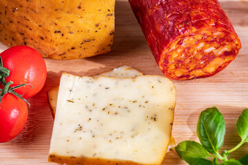 Sliced kulen and semi-hard cheese arranged neatly on a plate, garnished with fresh basil leaves. The vibrant colors of the red cured sausage, creamy-yellow cheese, and green basil create a visually ap