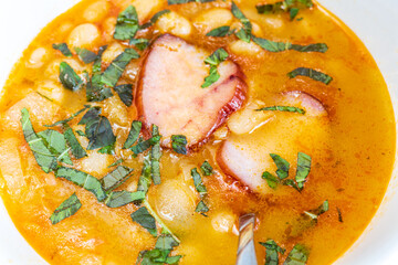 A hearty bowl of cooked bean stew with tender pieces of meat, served in a clean white dish. The warm, rich broth highlights the soft beans and juicy meat, while natural lighting 