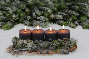 Vierter Advent: Adventskerzen in Grau, geschmückt mit Tannenzweigen und Beeren,  vor einem verschneiten Hintergrund aus Tannen.