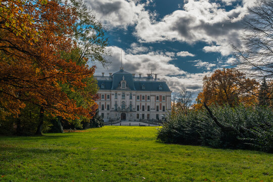 A picturesque view of a grand palace surrounded by vibrant autumn foliage under a dramatic sky, showcasing architectural elegance.