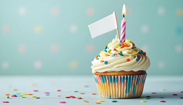 Festive cupcake with vanilla frosting and sprinkles. Candle and blank flag decorates sweet dessert. Bokeh lights adorn the background