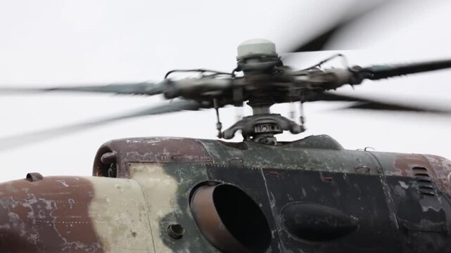 Aerial view of a military transport helicopter (Mi-8) landed in a vast, brown field during troop training operations, with mountains and solar panels visible.