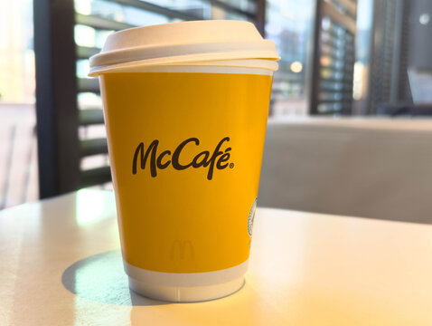 Villach, Austria - November 11, 2025: McCafe coffee cup on a table in a modern cafe setting, showcasing vibrant yellow branding and inviting atmosphere for coffee lovers