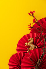 Golden horse statue on a red paper fan background with red plum blossoms against a bright yellow background. Ideal for Chinese New Year, year of the horse, or fortune themes.