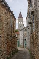 Fototapeta premium Stone Street in Old Town Village With Church Tower Under Cloudy Sky, Grohote, Solta
