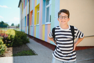 Smiling student wearing backpack posing near colorful school building