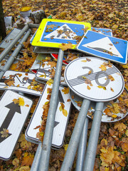 Autumn leaves cover piles of road signs and posts.