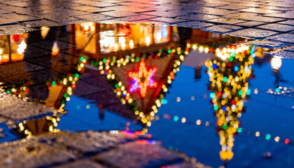 Christmas market reflected in puddle with colorful distortions. Urban holiday abstract.