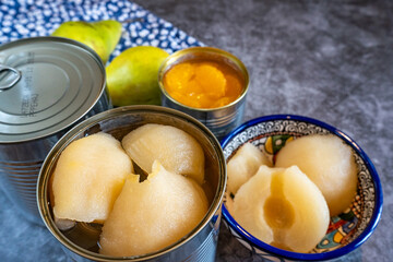 Canned pears and mandarin segments contrasted with two fresh pears, arranged on a rustic background. 