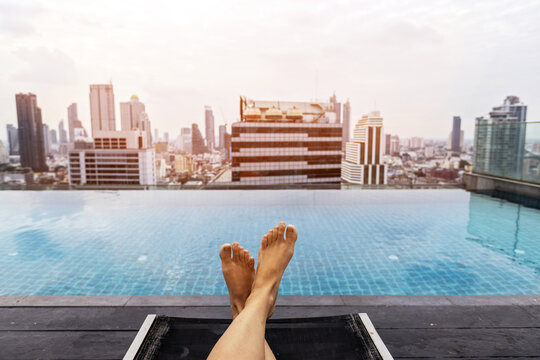feet near rooftop infinity pool in Bangkok city, tourist relaxing near swimming pool with the view of skyscraper buildings, Thailand - Powered by Adobe