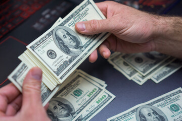 pair of hands counting a large stack of one hundred dollar bills on a dark laptop keyboard earning, budgeting, and financial planning concept of personal accounting, remote work, online trading