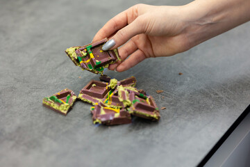 Woman's hand holds piece of Dubai chocolate on gray background. Green kadayif and pistachio spread with pistachio in trend dessert. Close-up, selective focus. High quality photo