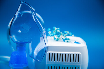 Close-up side view of a blue mask and a device on a blue background and flowers nearby. The concept of treating respiratory diseases, lung diseases, prevention and self-care. High quality photo