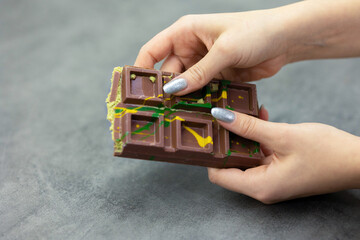 Female hands breaking off piece of Dubai chocolate on gray background. Green kadayif and pistachio spread with pistachio in trend dessert. Close-up, selective focus. High quality photo