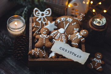 Concept of home christmas or new year celebration, family traditions. Assortment of gingerbread cookies with icing in a vintage wooden box on a window sill with atmospheric lights