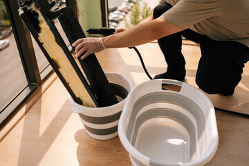 Cropped shot of technician male using a steam cleaner to clean air conditioner parts placed in bucket, ensuring proper hygiene and maintenance. Concept of maintenance modern home appliance.