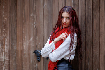 Fototapeta premium Young woman posing in front of wooden door with red scarf