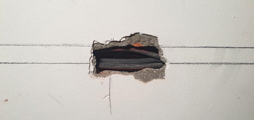 Small, rectangular opening in a white plastered wall showing black electrical cables and underlying brickwork, following marked guide lines for installation