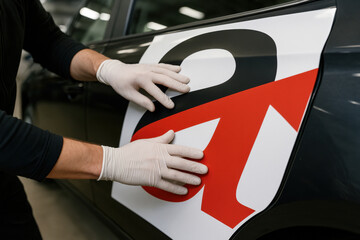 Applying Vinyl to Car: A technician's gloved hands delicately apply a vibrant vinyl graphic onto a sleek car, showcasing precision and care in detailing.