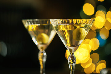 A close-up shot of a classic martini glass with a green olive submerged in clear liquid, with dreamy golden holiday bokeh lights softly glowing in the background.