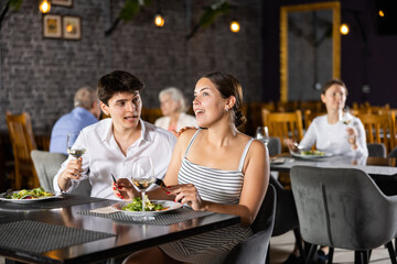 Happy young couple having romantic dinner in restaurant. Laughing girl and guy enjoying conversation and drinking wine at table
