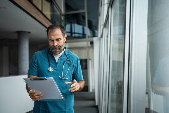 Mature male doctor reviewing medical clipboard in hospital corridor