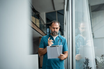 Male doctor in scrubs reviewing patient records on clipboard