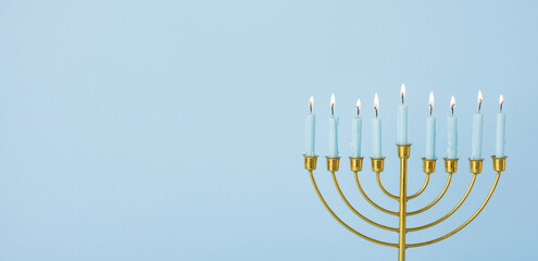 A golden menorah with lit candles stands against a soft blue banner backdrop. The image captures...