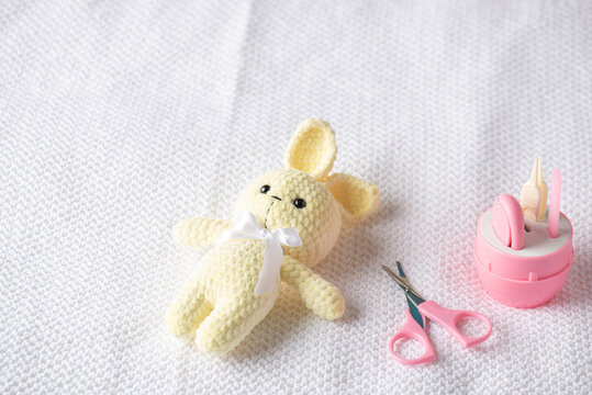 Soft knitted yellow teddy lies beside a pink baby grooming kit with scissors, suggesting tender maternity and newborn care and gentle parenting