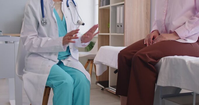 Patellar reflex examination by doctor in neurologist office. Medical specialist holding hammer to tap, check knee reflex and nervous system response of patient sitting on bed, explain diagnosis