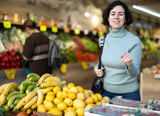 Female shopper carefully selects fresh bananas and other fruits in a grocery supermarket