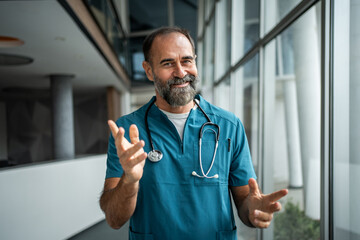 Mature male doctor wearing scrubs talking in hospital