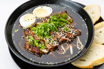 Black bowl of soy ramen with sliced pork, egg, scallions and sesame, isolated on white