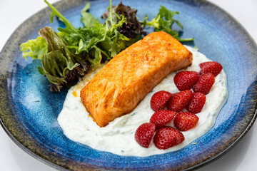 Seared salmon fillet with yogurt sauce, fresh strawberries and greens on blue ceramic plate