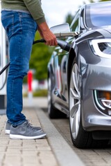 Man charging a sleek silver electric car at a public charging station on a bright day