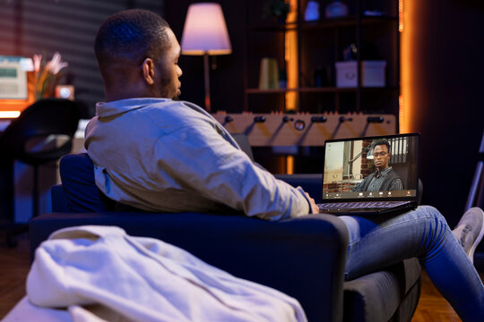 Focused black guy smiling and waving during a web conference in his living room, showcasing online discussion in a digital and wireless lifestyle. Conference speaker with attendees on call.