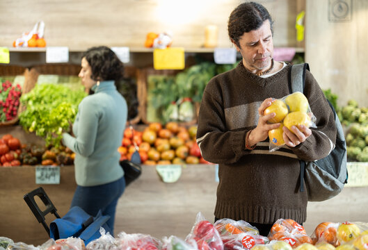 Adult man buyer choosing fresh apples in plastic bag in vegetable shop