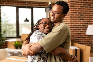 African american couple sharing warm embrace in brick wall apartment, celebrating newly purchased...