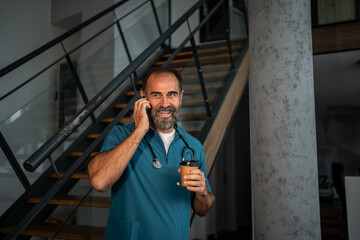 Mature doctor talking on phone drinking coffee during break