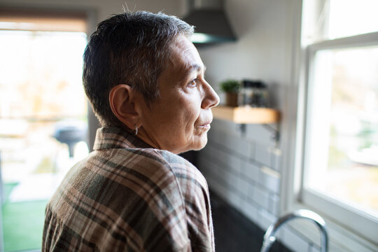 Senior woman gazing thoughtfully by kitchen window at home