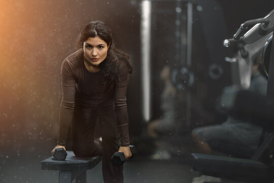 Sportive Latina girl working out with dumbbell in well-equipped gym during weight training session