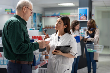 Obraz premium Senior patient in a dispensary listens to a pharmacist advice on cardiovascular care. Surrounded by pharmacy products, old man learns about prescription medication for heart health and wellness.