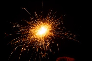 Bright sparkler emitting vibrant golden sparks against a dark background, creating a festive...