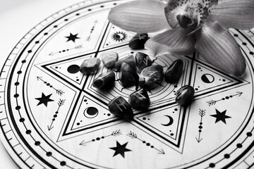 Scandinavian amethyst runes on a wooden altar for divination and an orchid flower. Black and white photo. Fortune telling, witchcraft, and spiritual esoteric practice.